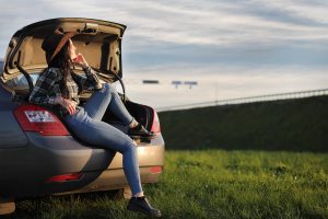 A cowgirl sits on the back of a sedan in the New Mexico countryside after getting title loans in Sapulpa