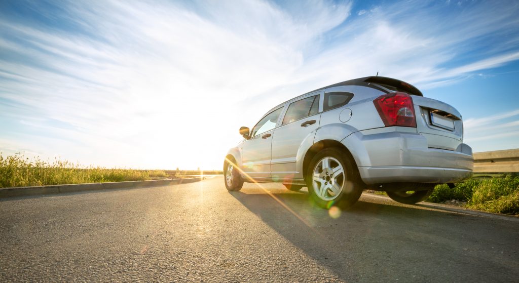 A white sedan drives down a Texas country road during sunrise.